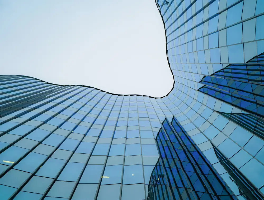 Blue glass facade seen from the ground, opening onto the sky